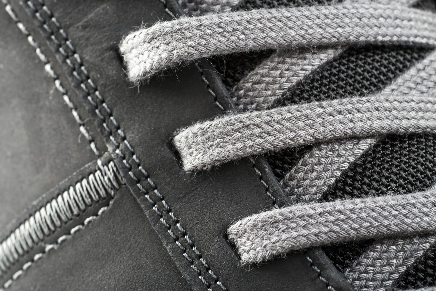 Macro detail of a sneaker: contrast stitching through nubuck, a woven lace and the mesh panel behind it.